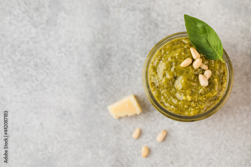 Pesto sauce in a jar with pine nuts, a slice of parmesan and green basil leaves. Top view. Copy space.