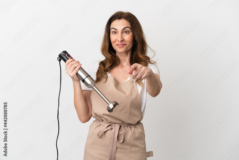 Middle aged caucasian woman using hand blender isolated on white background surprised and pointing front Middle aged caucasian woman using hand blender isolated on white background surprised and pointing front