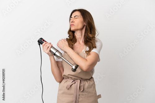 Middle aged caucasian woman using hand blender isolated on white background suffering from pain in shoulder for having made an effort