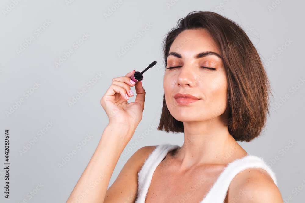 Beautiful woman with makeup hold black mascara brush on gray background, beauty concept Beautiful woman with makeup hold black mascara brush on gray background, beauty concept