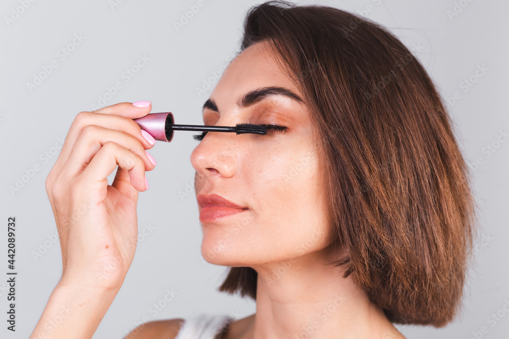 Beautiful woman with makeup hold black mascara brush on gray background, beauty concept Beautiful woman with makeup hold black mascara brush on gray background, beauty concept
