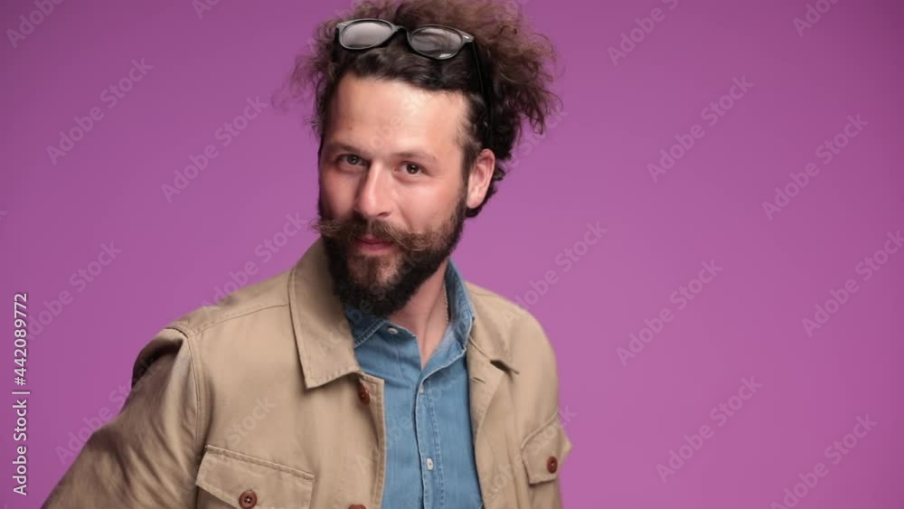 bearded curly hair guy with glasses on head pointing fingers, moving and dancing, spinning and having fun on pink background in studio