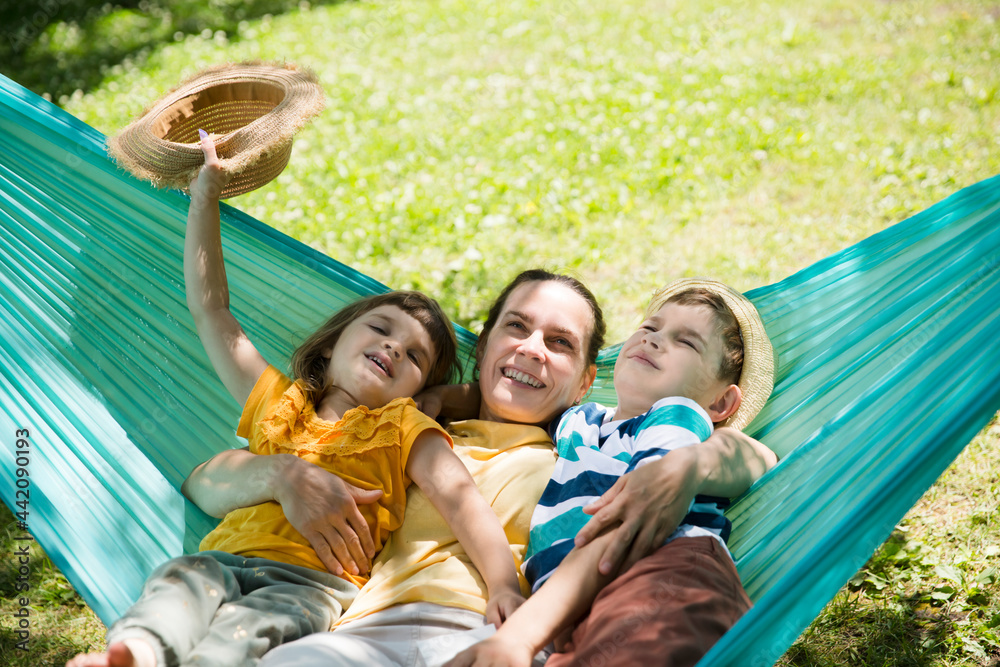 Fototapeta premium mom and Two kids swing in a hammock in a summer park or garden. Concept of friendly family.