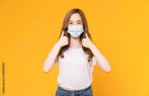 Asian woman wear masks to protect disease and showing thumbs up or like on yellow background.