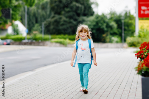 Cute little preschool girl going to playschool. Healthy toddler child walking to nursery and kindergarten. Happy child with backpack on city street, outdoors. City, traffic, safety on school way.