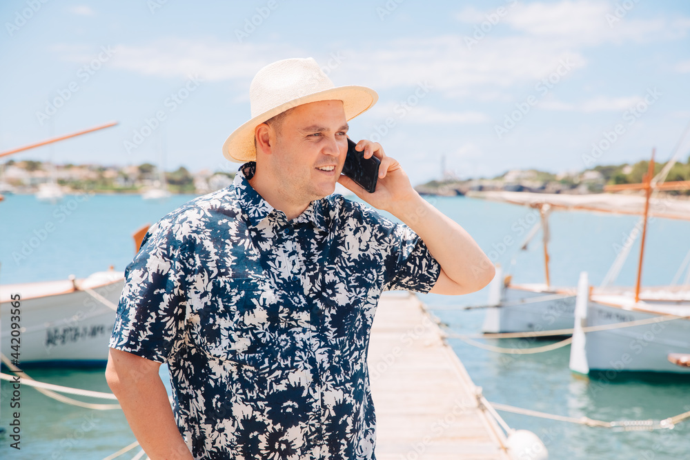 Happy man in straw hat by the sea, speaks on the cell phone . Harbor master is early at the jetty. Enjoy vacation by the sea 