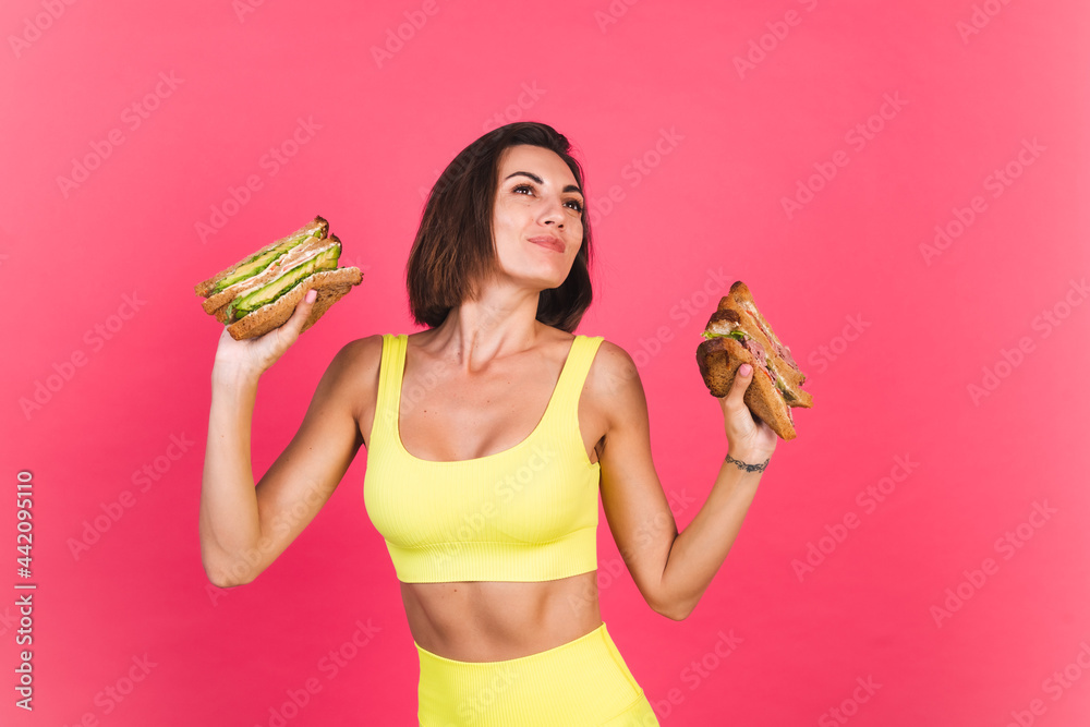 Beautiful fit woman in yellow bright fitting sportswear on pink background happy hold healthy avocado and roast beef sandwich Beautiful fit woman in yellow bright fitting sportswear on pink background happy hold healthy avocado and roast beef sandwich