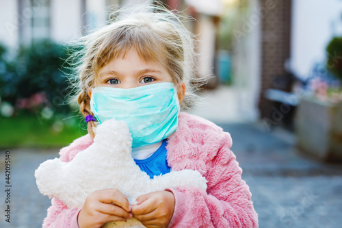 little toddler girl in medical mask as protection against pandemic coronavirus quarantine disease. Cute child using protective equipment as fight against covid 19 and holding bear toy.