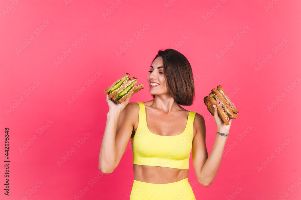 Beautiful fit woman in yellow bright fitting sportswear on pink background happy hold healthy avocado and roast beef sandwich