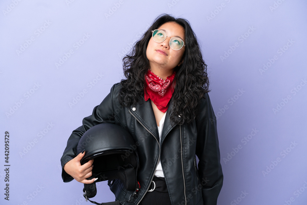 Young asian woman with a motorcycle helmet isolated on purple background and looking up Young asian woman with a motorcycle helmet isolated on purple background and looking up