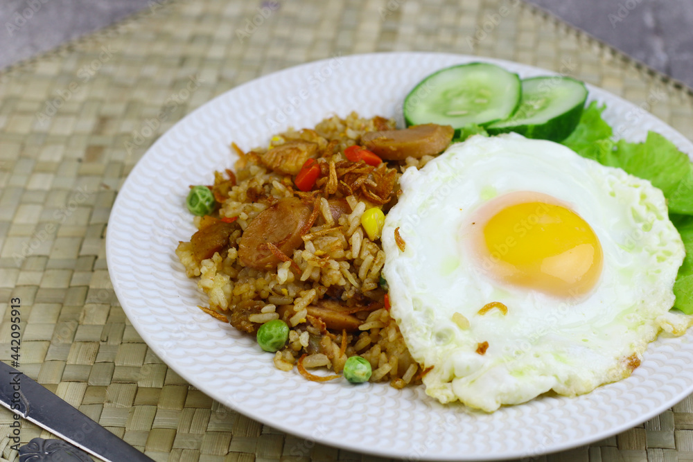 Nasi Goreng or Fried Rice, one of Indonesian popular food, topping with sunny side up egg, cucumber slices, lettuce and crackers. Top view, copy space for text. Nasi Goreng or Fried Rice, one of Indonesian popular food, topping with sunny side up egg, cucumber slices, lettuce and crackers. Top view, copy space for text.