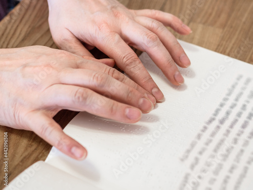 female fingers read book with braille and usual text closeup on wooded table