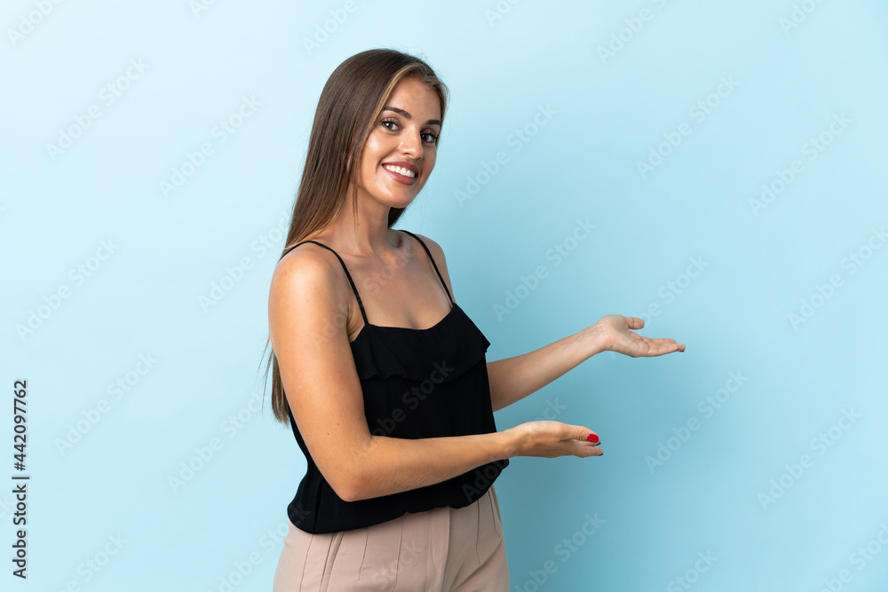 Young Uruguayan woman isolated on blue background extending hands to the side for inviting to come Young Uruguayan woman isolated on blue background extending hands to the side for inviting to come