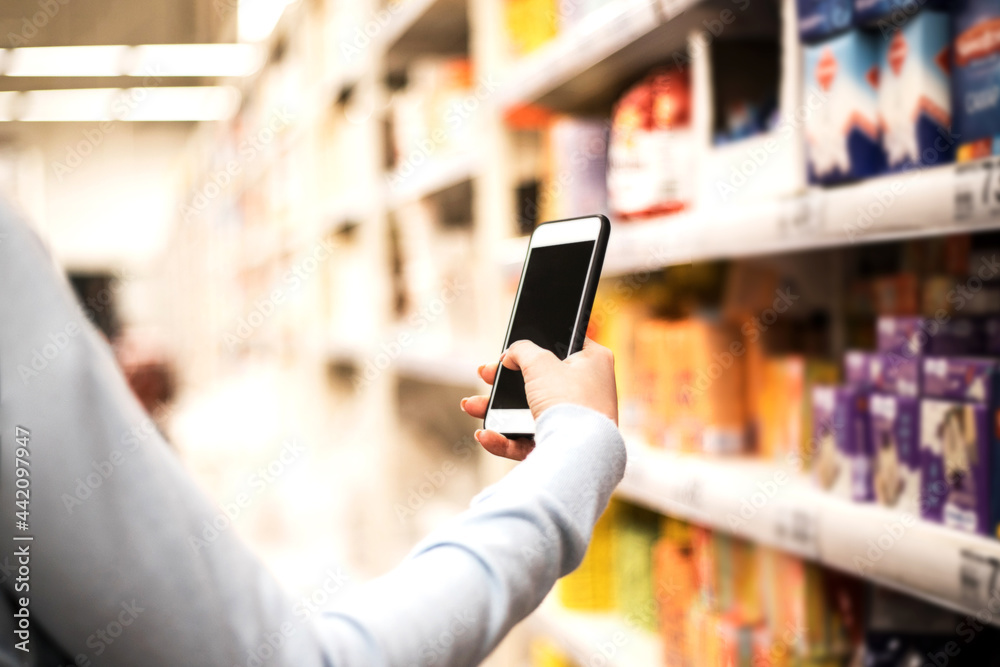 Woman's hand holding smart phone on supermarket blur background. Woman's hand holding smart phone on supermarket blur background.