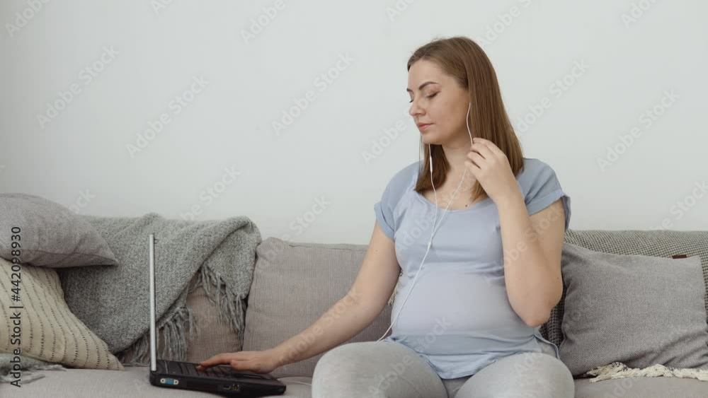 A pregnant woman in home clothes is sitting on a sofa and using a laptop. Third trimester of pregnancy. Preparation for childbirth and care of the newborn baby A pregnant woman in home clothes is sitting on a sofa and using a laptop. Third trimester of pregnancy. Preparation for childbirth and care of the newborn baby