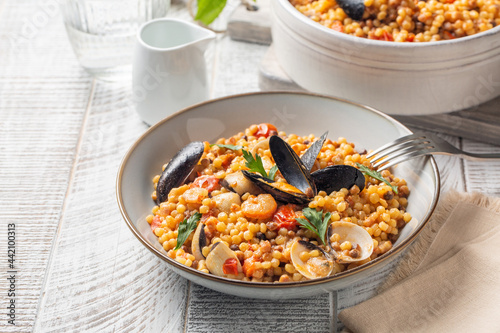 Italian pasta. Fregula with seafood on a white wood surface.
