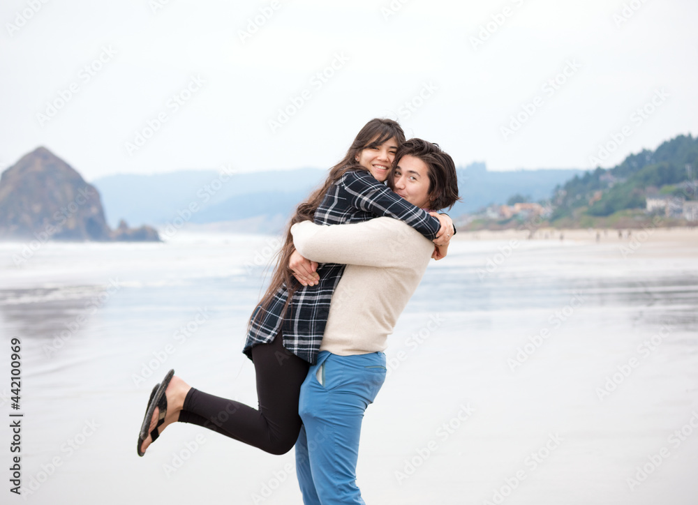 Young man lifting smiling woman up on beach by ocean