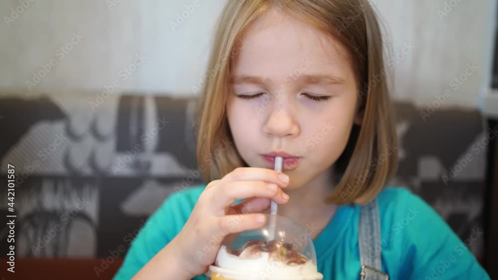 Funny little girl drinks a cold drink through a tube in a cafe. children's menu. milkshakes and soda. baby food. Funny little girl drinks a cold drink through a tube in a cafe. children's menu. milkshakes and soda. baby food.