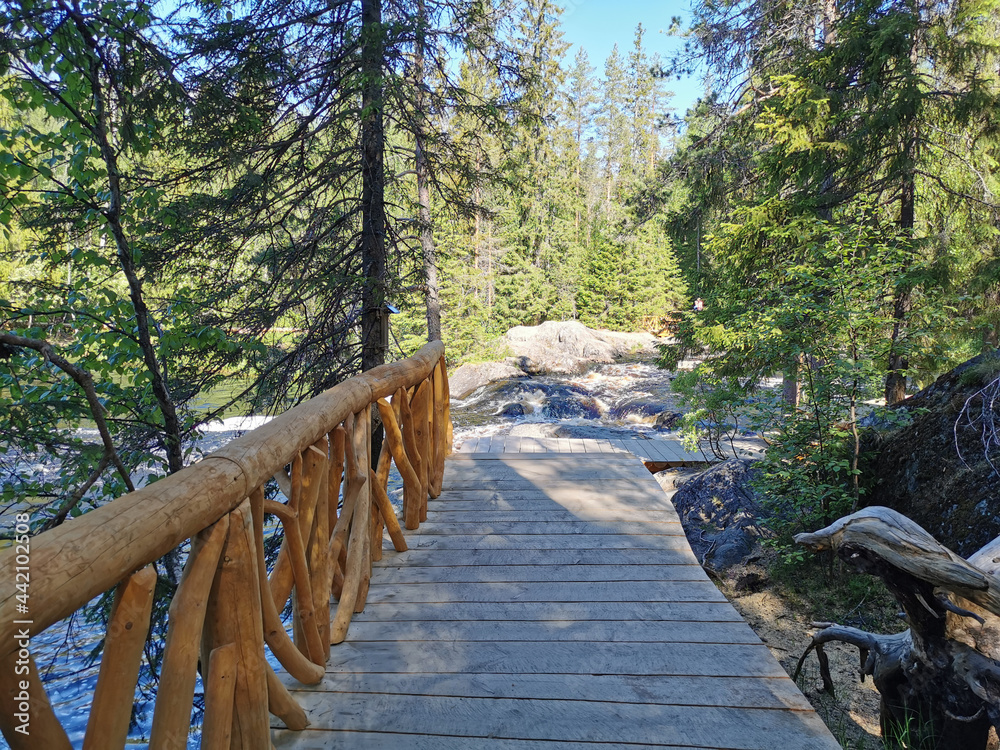Obraz premium Wooden flooring with original railings leading to the waterfalls of the Tohmajoki River in Karelia on a sunny summer morning..