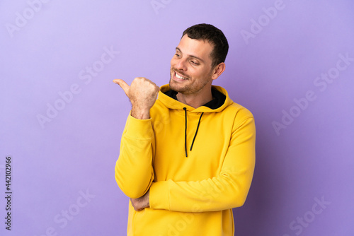 Brazilian man over isolated purple background pointing to the side to present a product