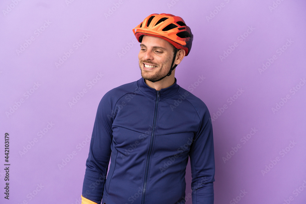 Young Brazilian cyclist man isolated on purple background looking to the side and smiling - obrazy, fototapety, plakaty 