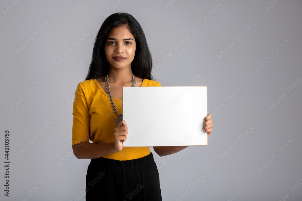 A young girl or businesswoman holding a signboard in her hands on a gray background. A young girl or businesswoman holding a signboard in her hands on a gray background.