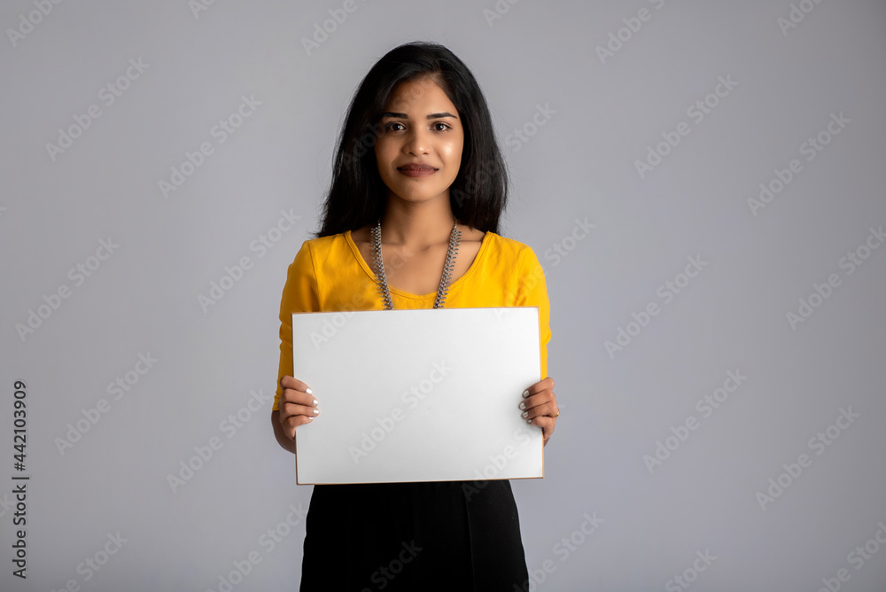 A young girl or businesswoman holding a signboard in her hands on a gray background. A young girl or businesswoman holding a signboard in her hands on a gray background.