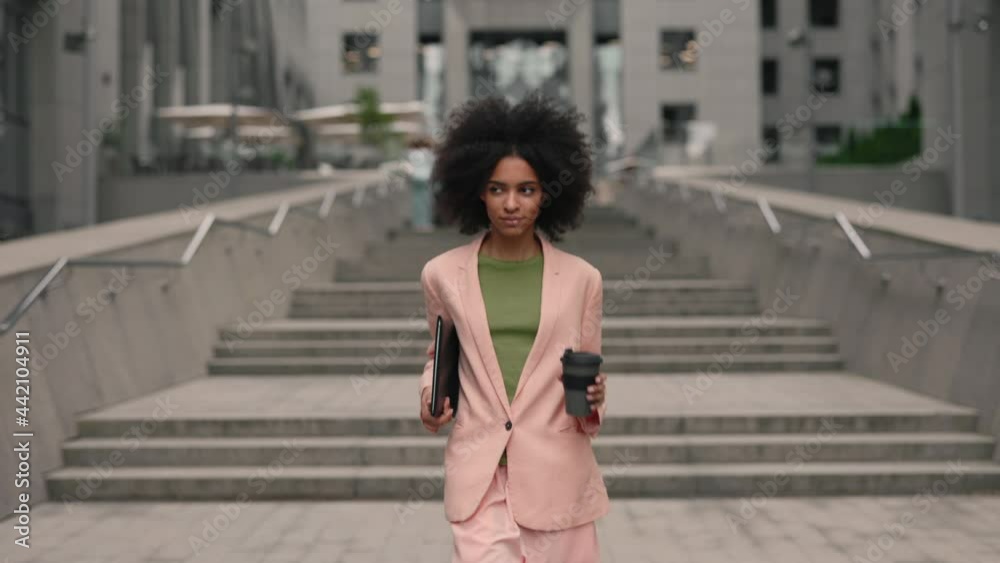 Successful young beautiful multiracial woman with documents under her hand and smartphone walking between business buildings and smiling with joy. Attractive business girl and career people concept. Successful young beautiful multiracial woman with documents under her hand and smartphone walking between business buildings and smiling with joy. Attractive business girl and career people concept.