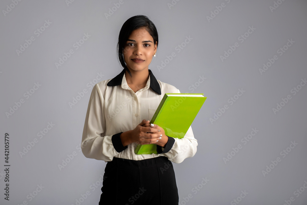 Pretty young girl holding book and posing on grey background