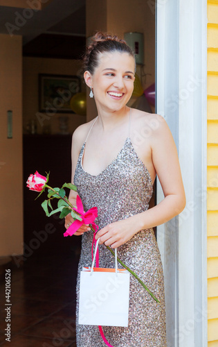 Happy Girl Graduate is Standing on the Porch Smiling Holding Empty Bag and Rose