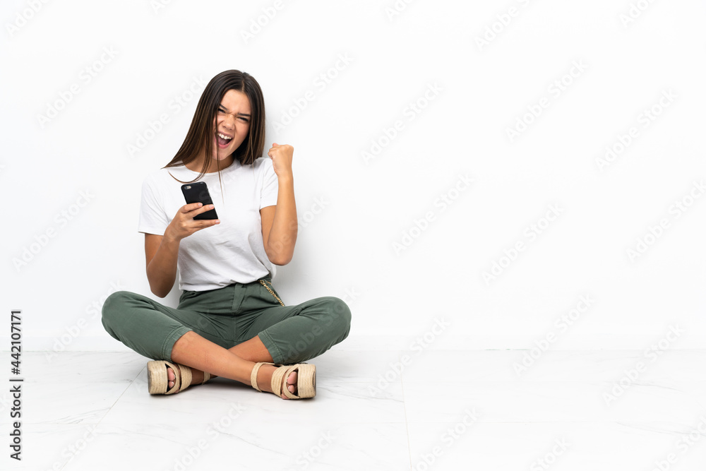 Teenager girl sitting on the floor with phone in victory position Teenager girl sitting on the floor with phone in victory position