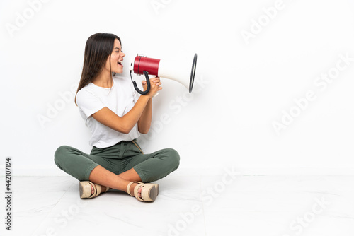 Teenager girl sitting on the floor shouting through a megaphone