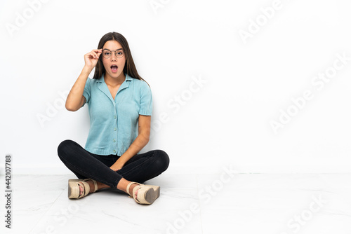 Teenager girl sitting on the floor with glasses and surprised