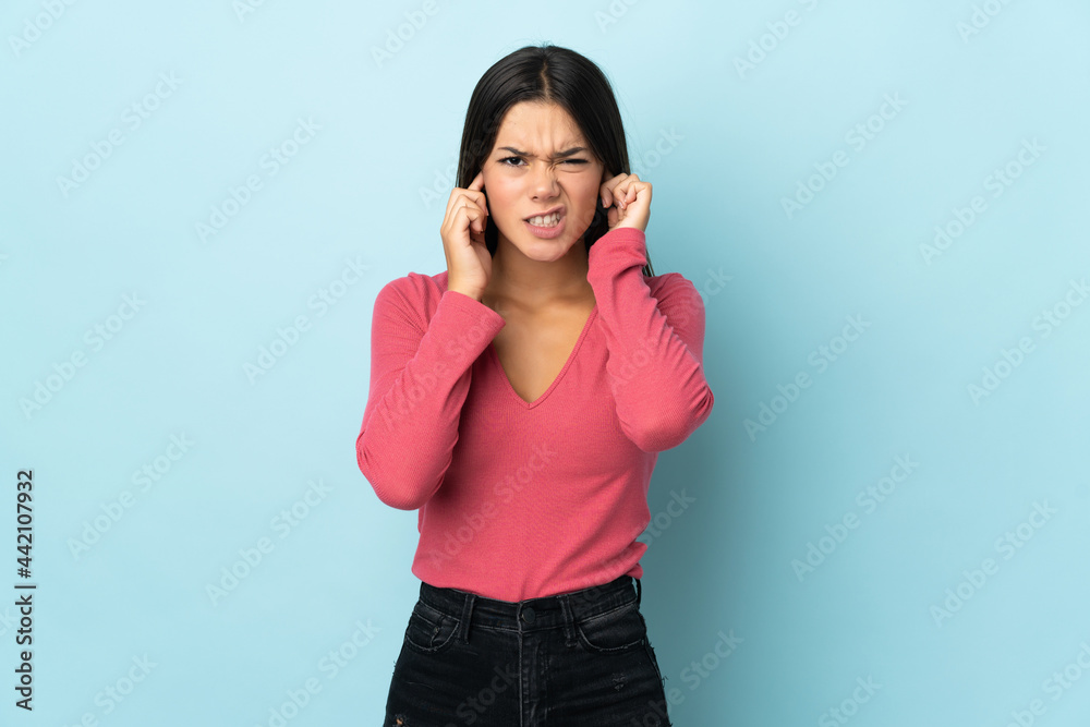 Teenager girl isolated on blue background frustrated and covering ears Teenager girl isolated on blue background frustrated and covering ears