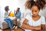Upset African American girl sitting alone in armchair, parents quarreling on background, preschooler crying daughter suffering from mother and father quarrels, problem in family break up bad relations