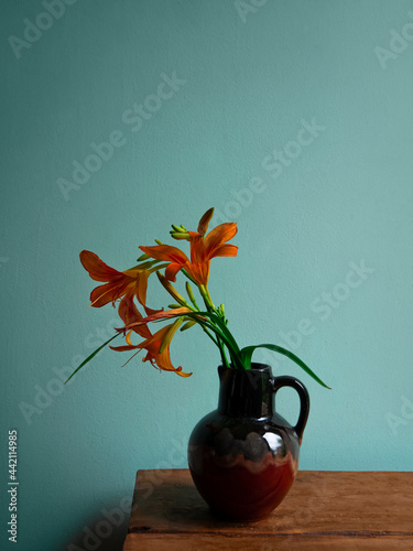 Tiger lily in ceramic vase with shadow turquoise wall background. Lilium lancifolium orange flowers bouquet on wooden farmhouse table. Summer cottagecore aesthetic country rural minimalism dark style.