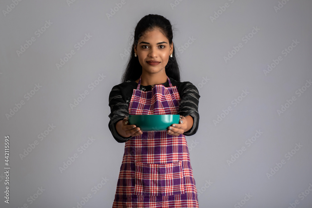 Young girl holding and posing with kitchen utensils pan on a grey background Young girl holding and posing with kitchen utensils pan on a grey background