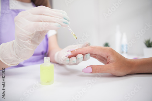Professional manicurist applying cuticle oil on fingers of female client