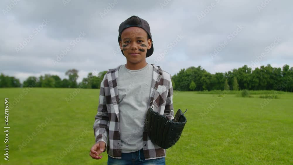 Concentrated confident cute school age boy pitcher in casual clothes with ball and baseball glove ready for a pitch, making hand gesture while playing baseball game on green field in public park. Concentrated confident cute school age boy pitcher in casual clothes with ball and baseball glove ready for a pitch, making hand gesture while playing baseball game on green field in public park.