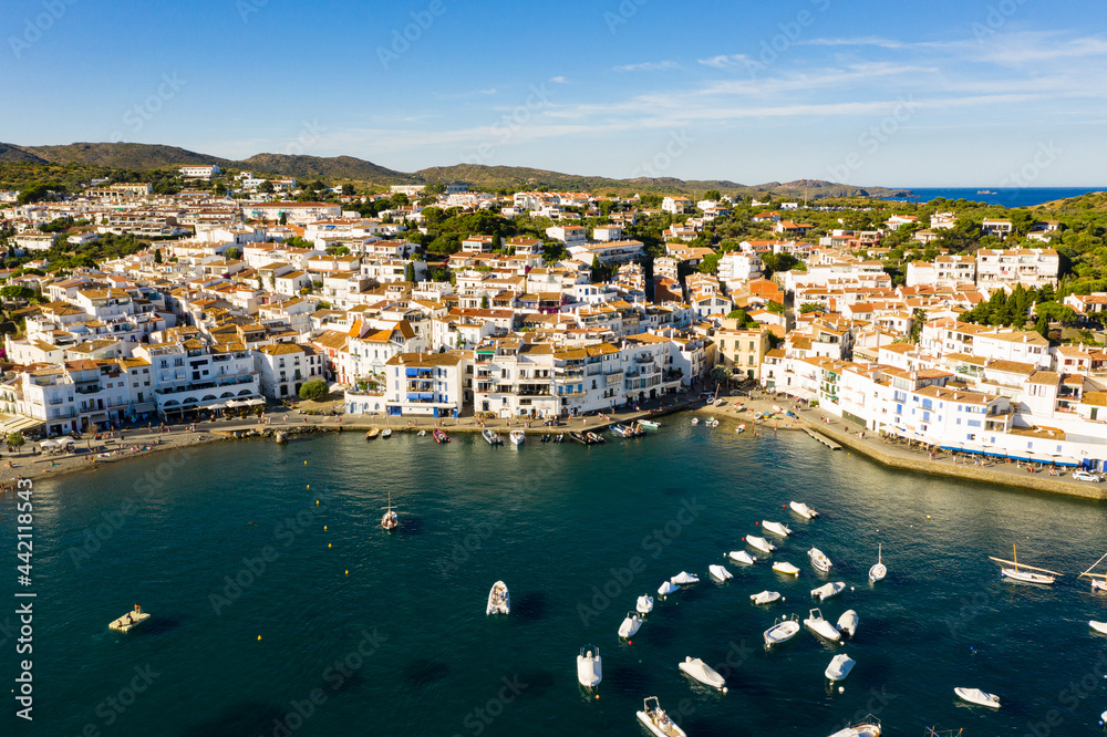 Scenic aerial view of Cadaques shoreline overlooking white buildings and boats parked in bay in summer, Catalonia, Spain