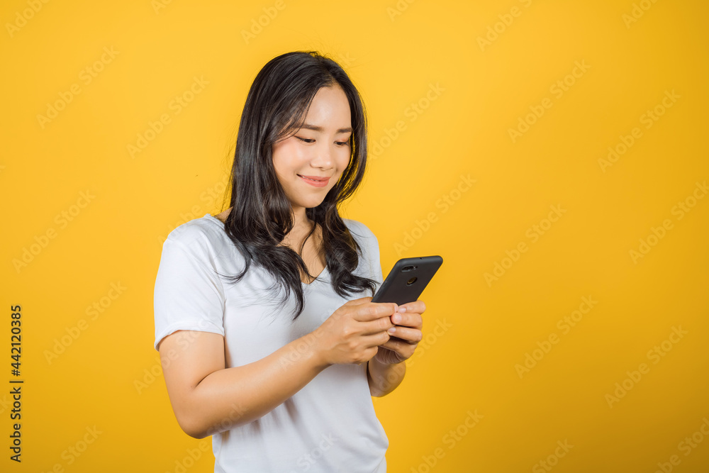 Portrait of smiling Asian woman wears white t-shirt using a smartphone isolated on yellow background Portrait of smiling Asian woman wears white t-shirt using a smartphone isolated on yellow background