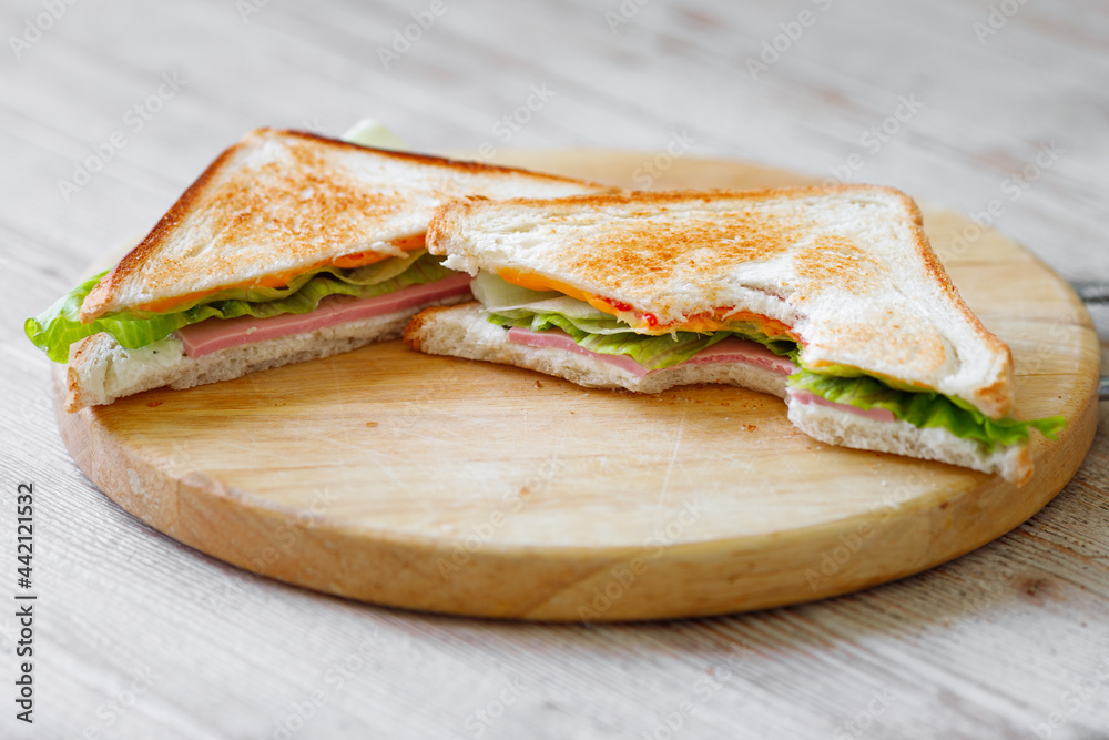 The cut sandwich lies on a wooden board on the table. Breakfast