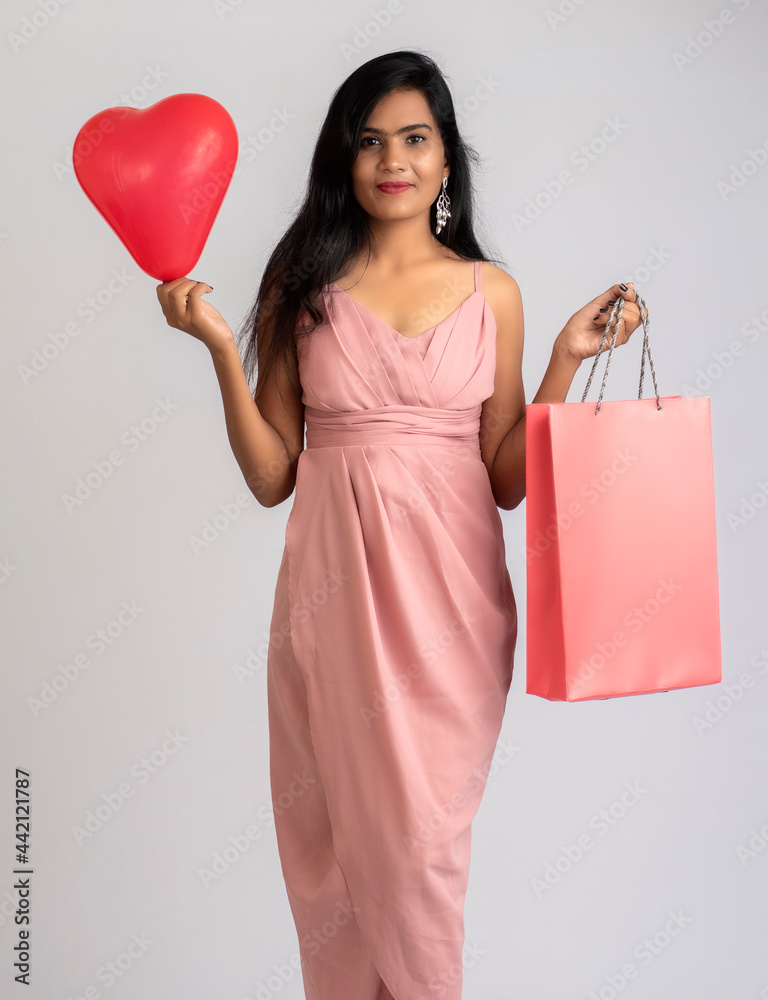 Beautiful young girl posing with shopping bags and balloon on a grey background Beautiful young girl posing with shopping bags and balloon on a grey background
