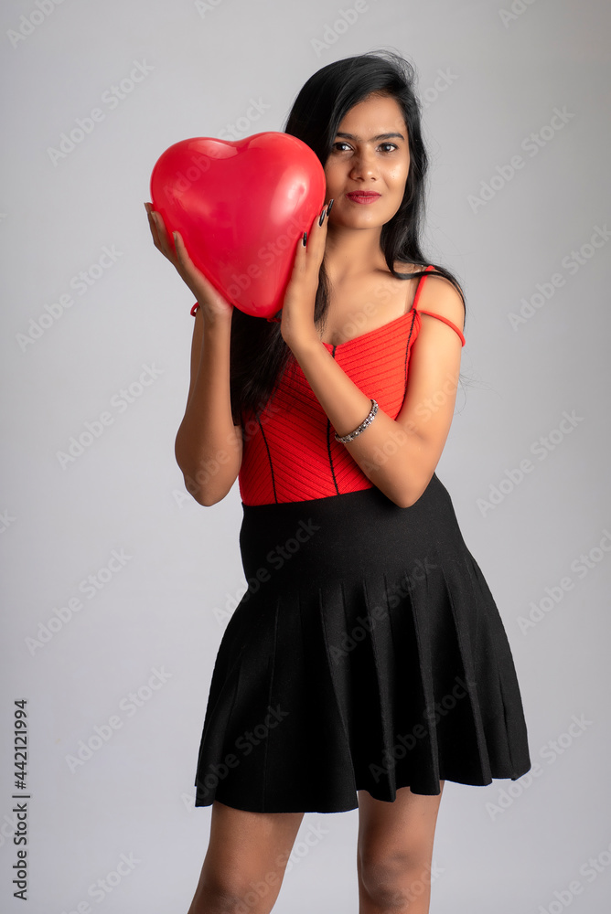 Cheerful cute girl in fancy red and black outfit posing with heart shape balloon.