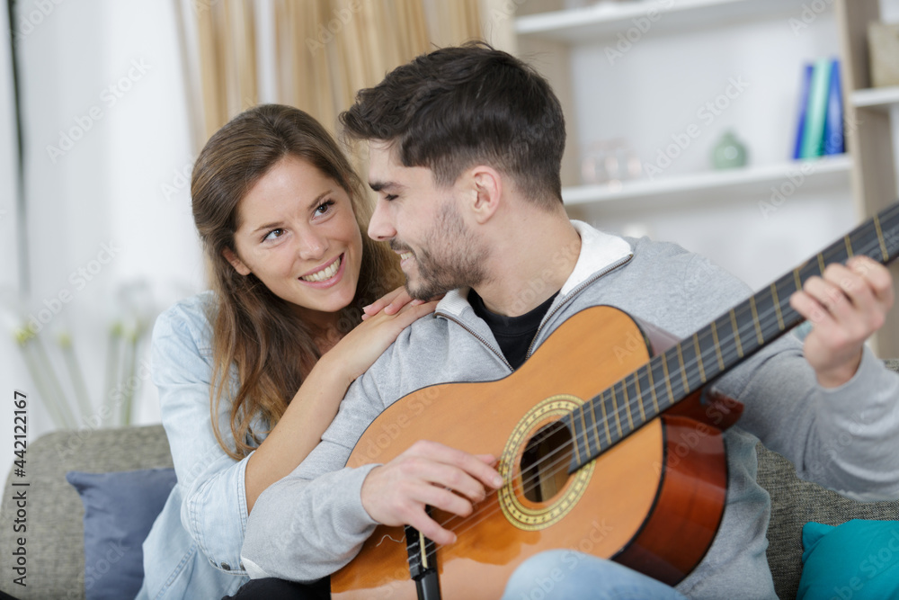 young couple playing guitar on couch indoor