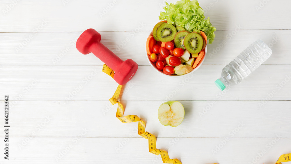 Select focus. Diet Health Planning and workout for new life. Sport exercise equipment workout gym. Dumbbells and measuring tape with fresh water, salad for healthy care, wood white background