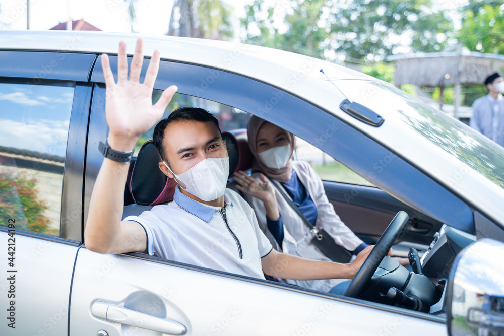 Muslim couple wearing masks waving from inside the car to the camera when they are going home