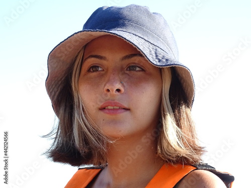 retrato rostro chica adolescente  rubia de pelo corto lacio con pecas ojos castaños en la playa con sombrero pituso azul y chaleco salvavidas naranja de fondo el agua de un lago photo