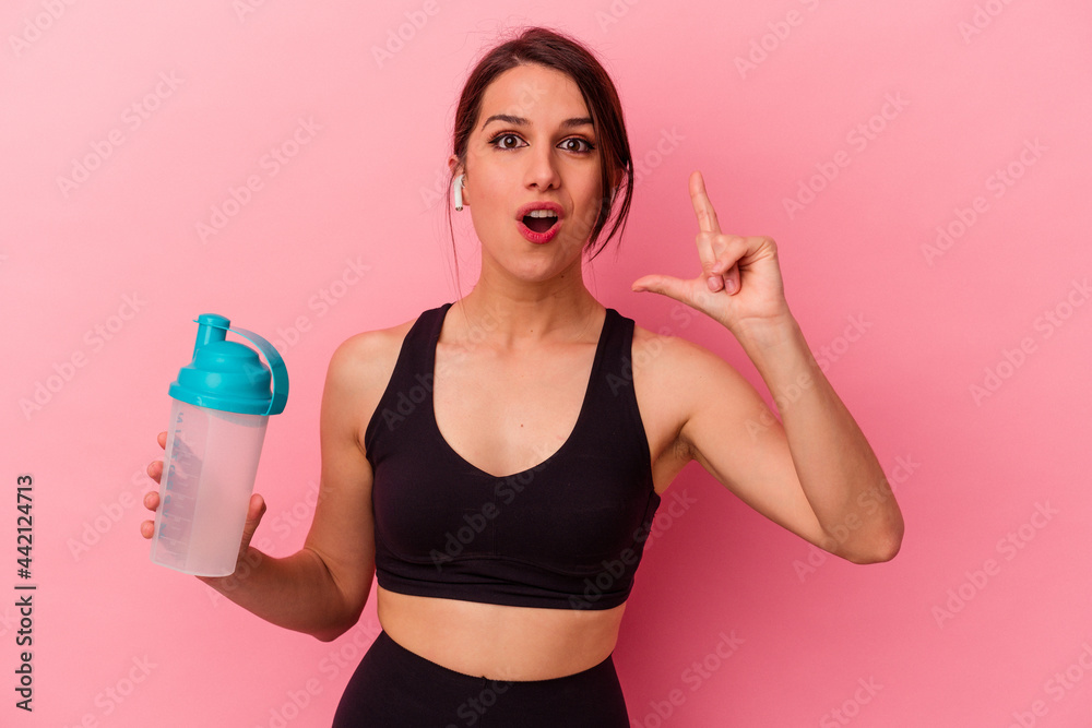 Young caucasian woman drinking a protein shake isolated on pink background having an idea, inspiration concept.