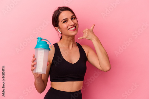 Young caucasian woman drinking a protein shake isolated on pink background showing a mobile phone call gesture with fingers.